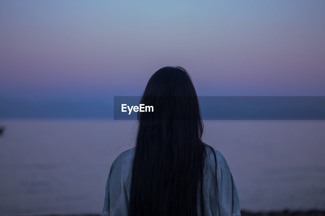 Rear view of woman standing against sea at sunset