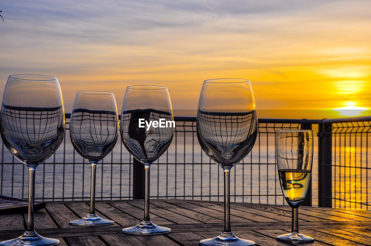 Close-up of wineglasses on table against sea during sunset