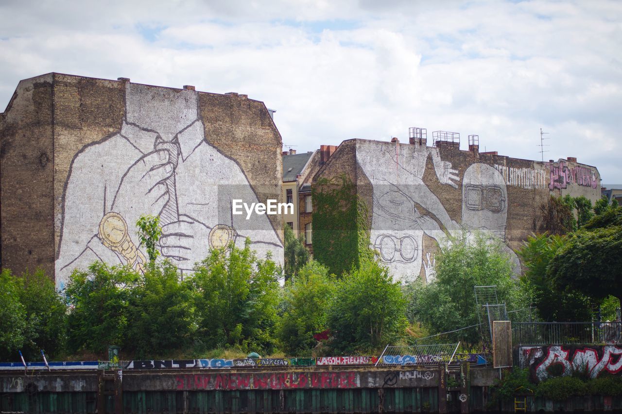 Low angle view of old building with mural against cloudy sky