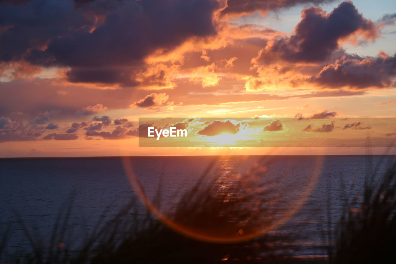 Scenic view of sea against cloudy sky during sunset