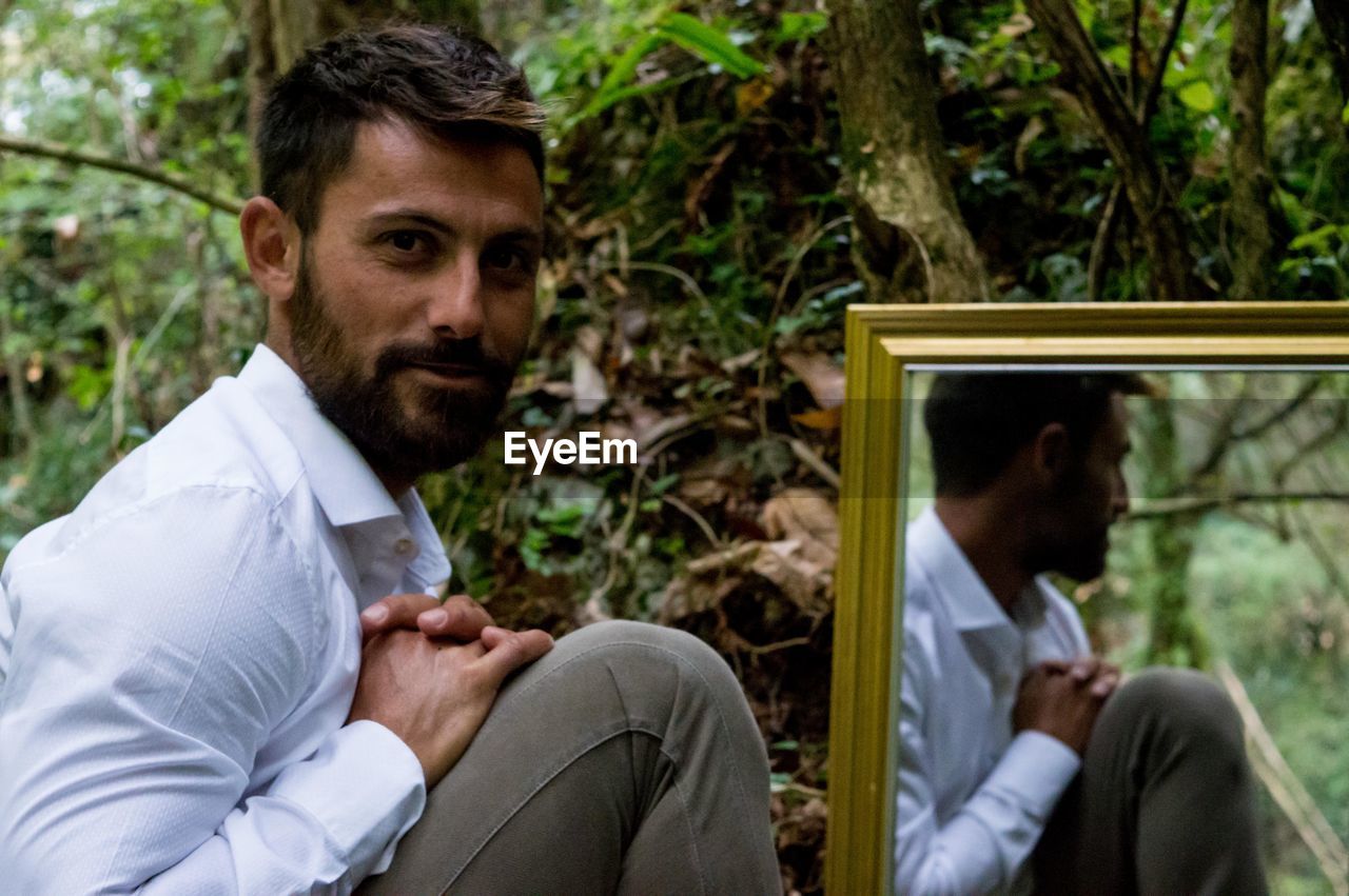 Portrait of young man with reflection on mirror at forest