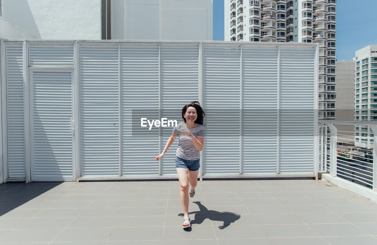 Full length of woman running against building in city