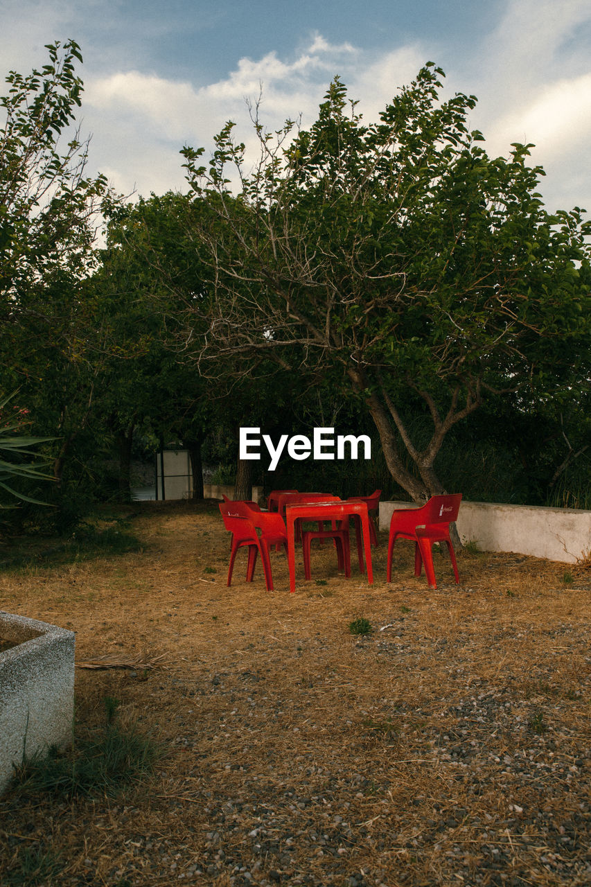 EMPTY CHAIRS AND TABLE BY TREES IN PARK AGAINST SKY