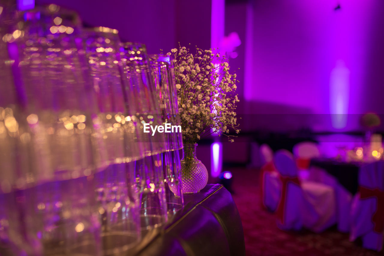 Glasses by vase on table in illuminated room