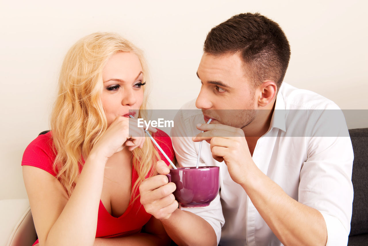 Loving couple sharing coffee from cup at home