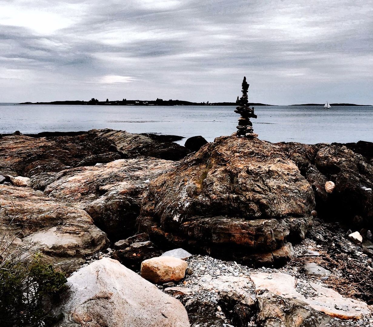 Stack of stones on rock against cloudy sky