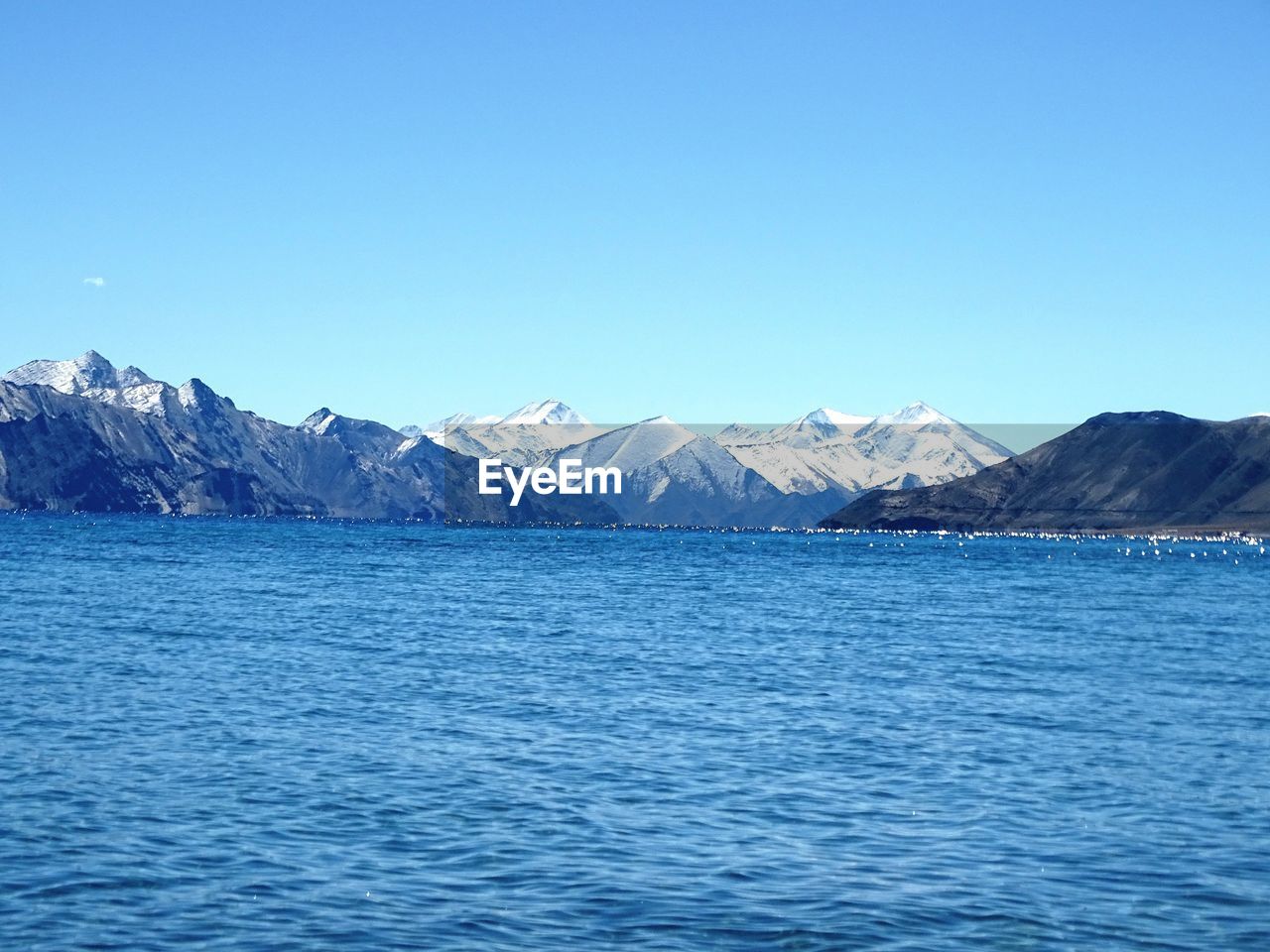 SCENIC VIEW OF SEA BY MOUNTAINS AGAINST CLEAR BLUE SKY