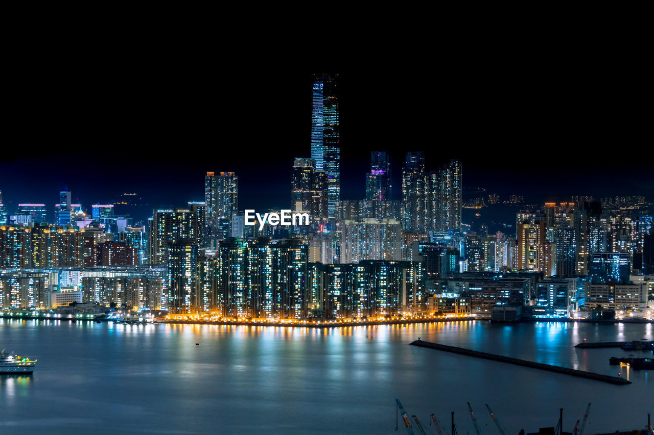 Illuminated buildings by river against sky at night