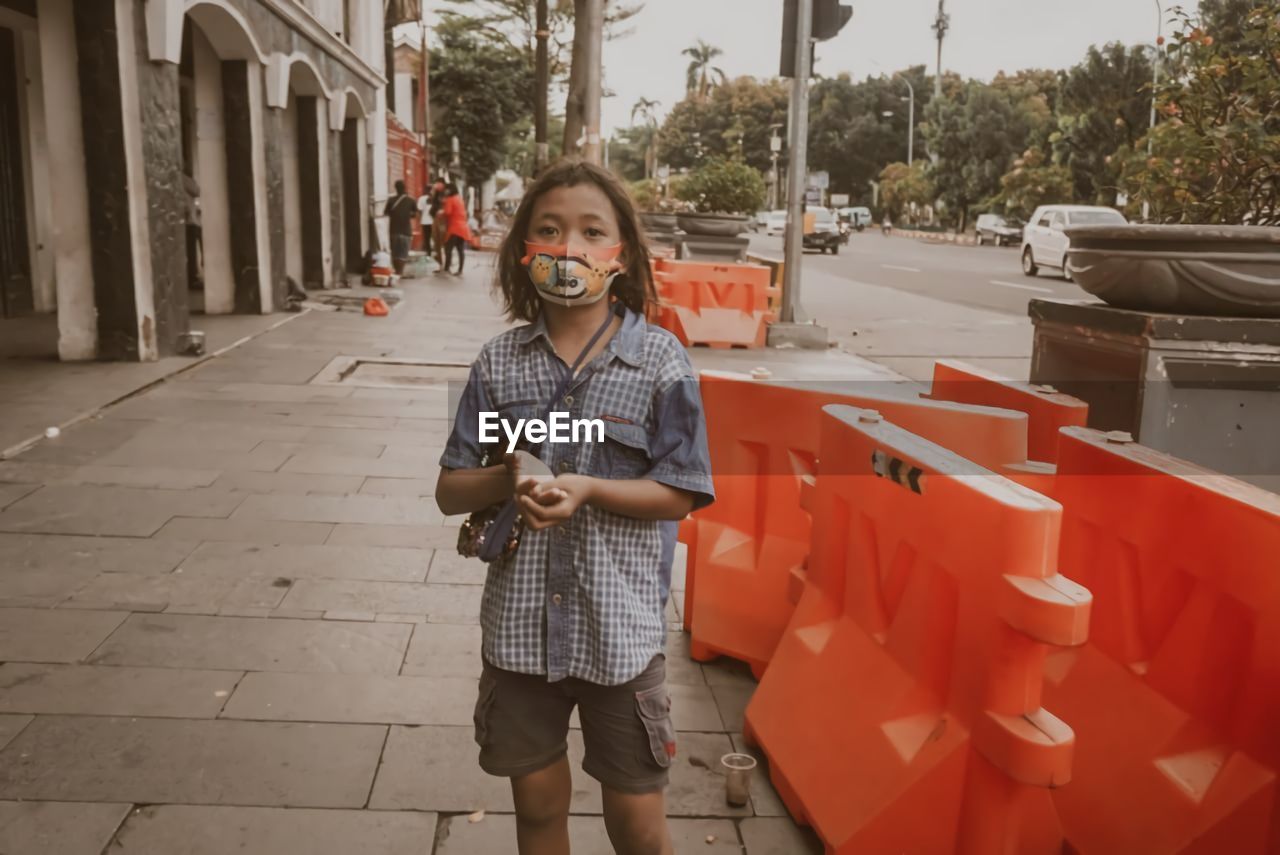 Portrait of teenage girl wearing mask begging on street