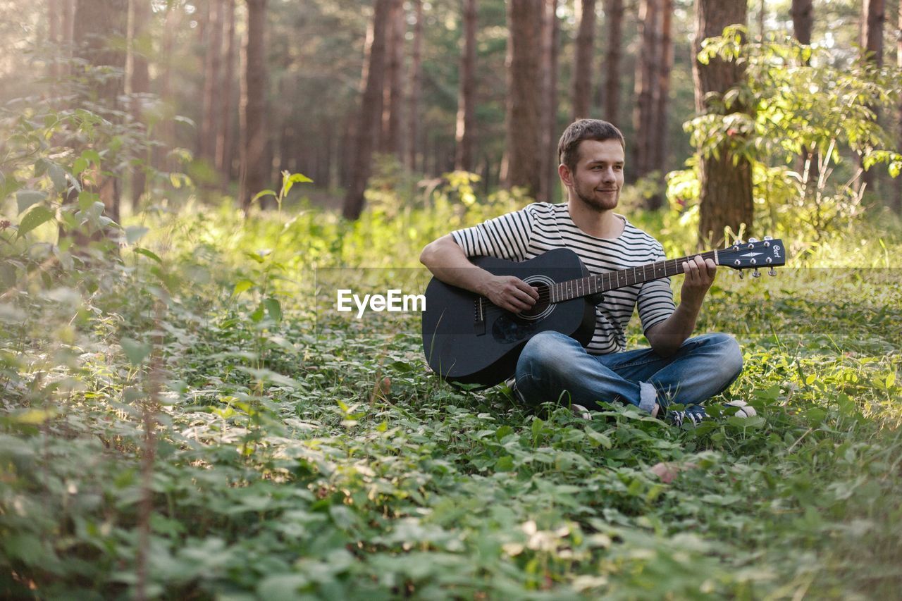 Young man playing guitar while sitting in forest