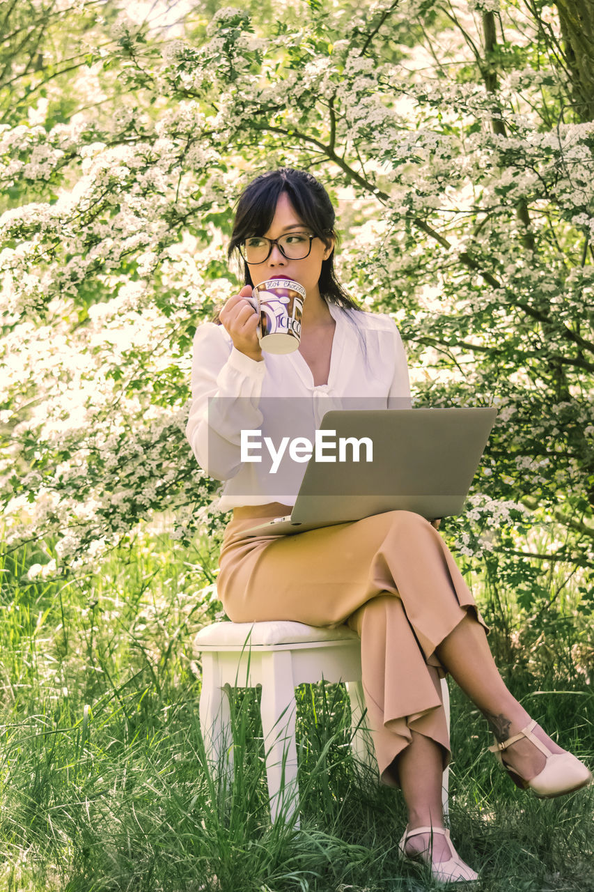 Woman holding laptop while sitting by plants