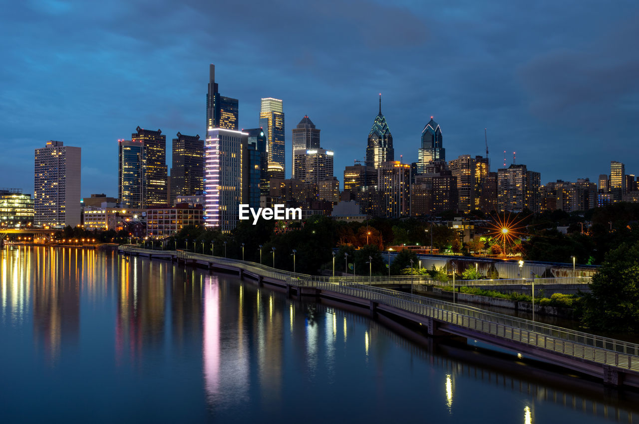 Illuminated buildings by river against sky in city at night