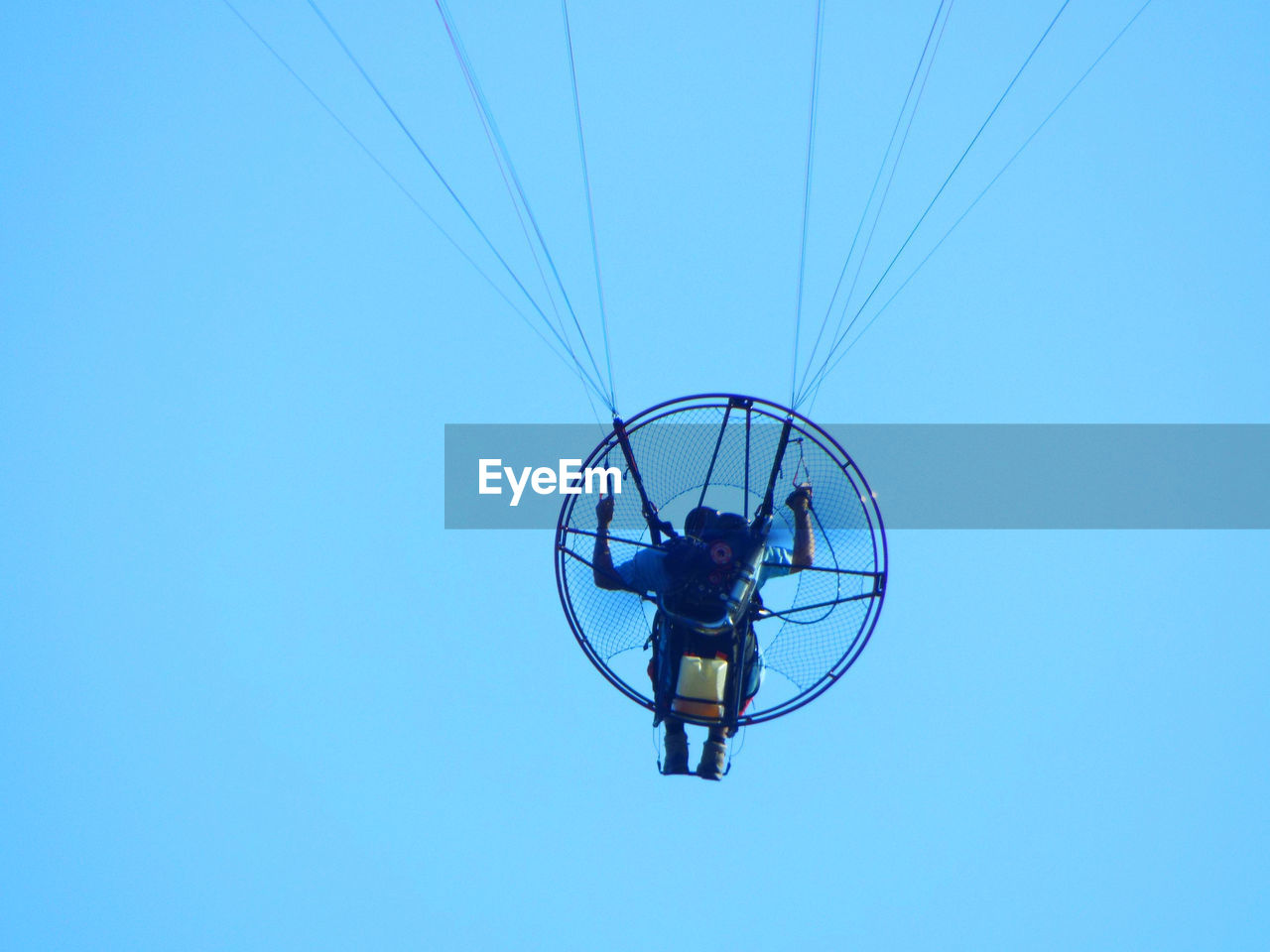 Low angle view of man paramotoring against clear blue sky