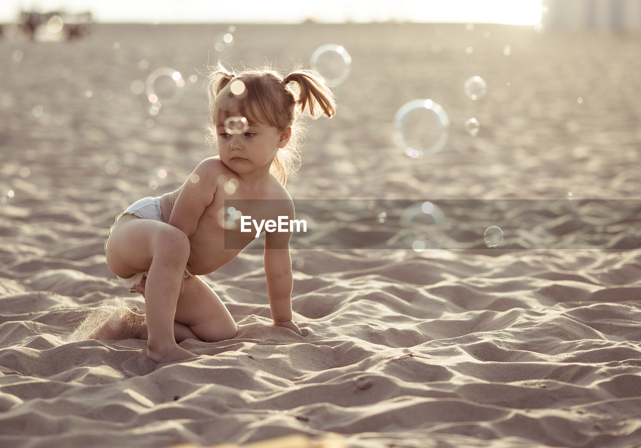 Cute girl playing with bubbles on sand at beach
