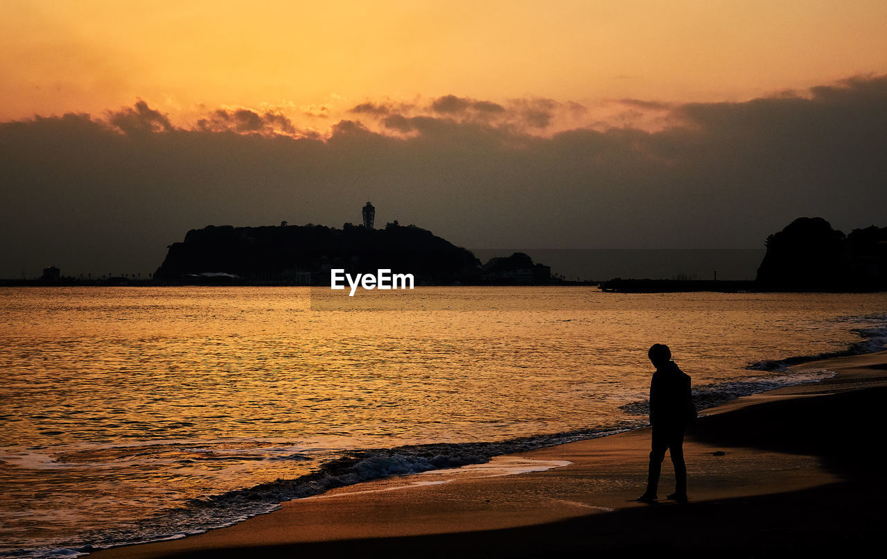 Silhouette man standing on beach against sky during sunset