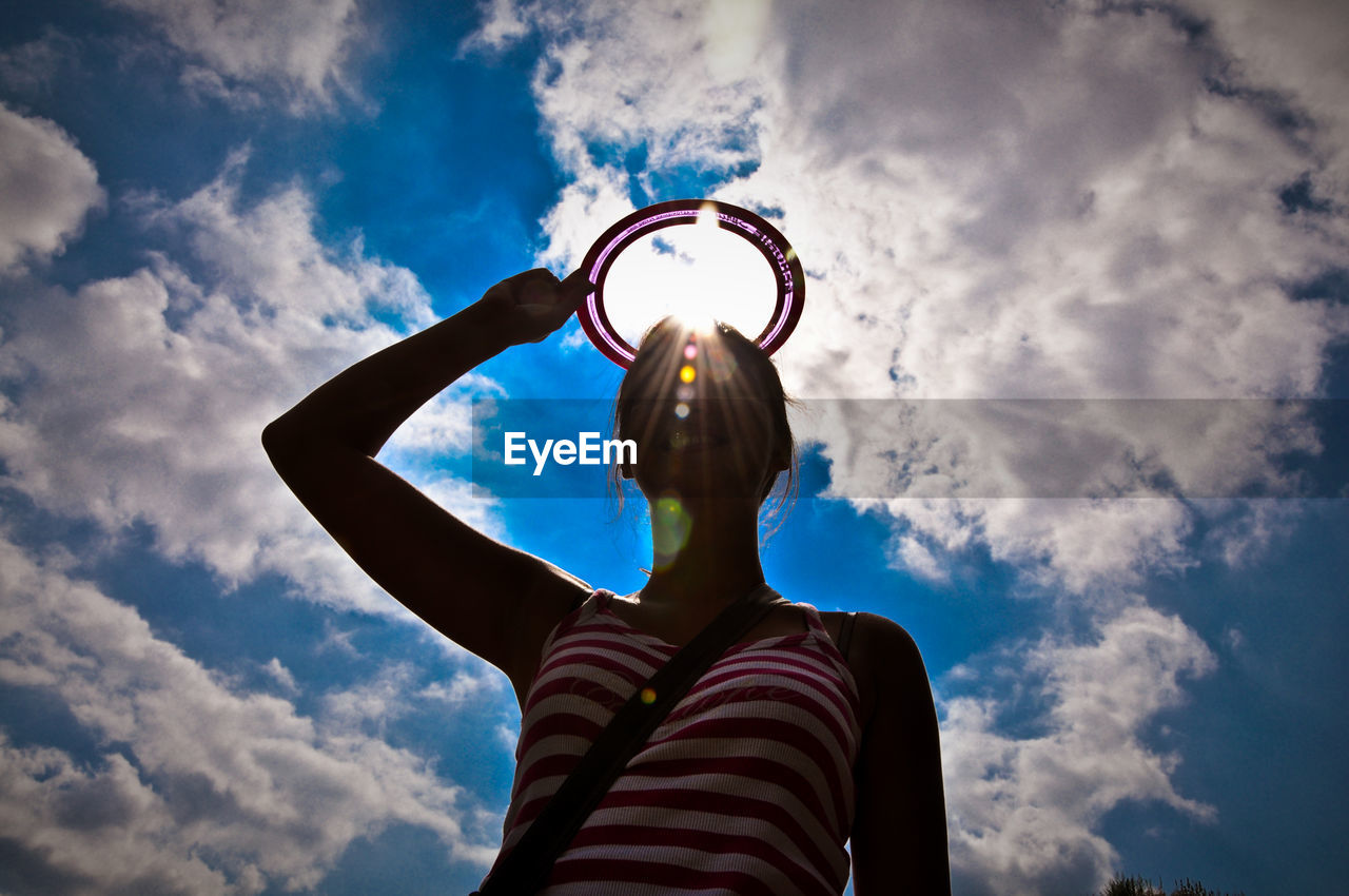 Low angle view of happy woman holding disc over head against cloudy sky