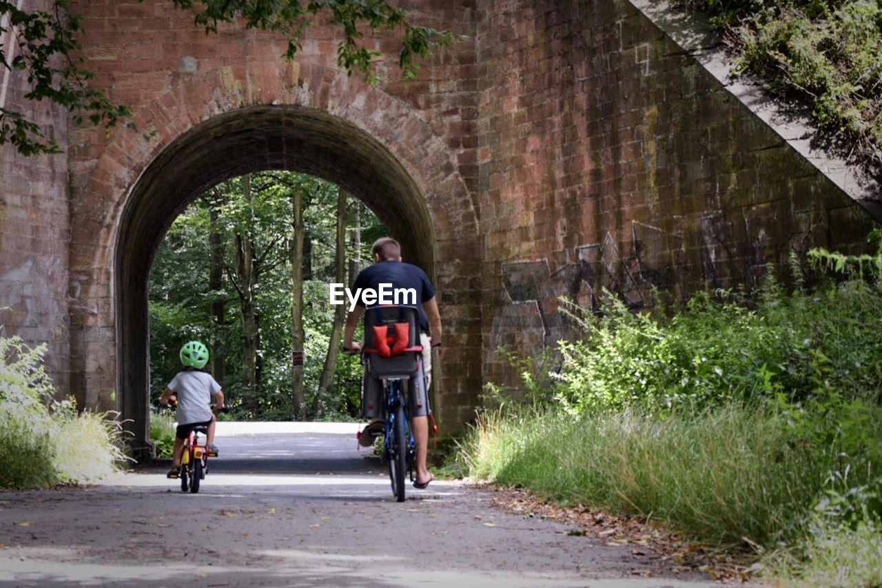 Rear view of father and son riding bicycle on road