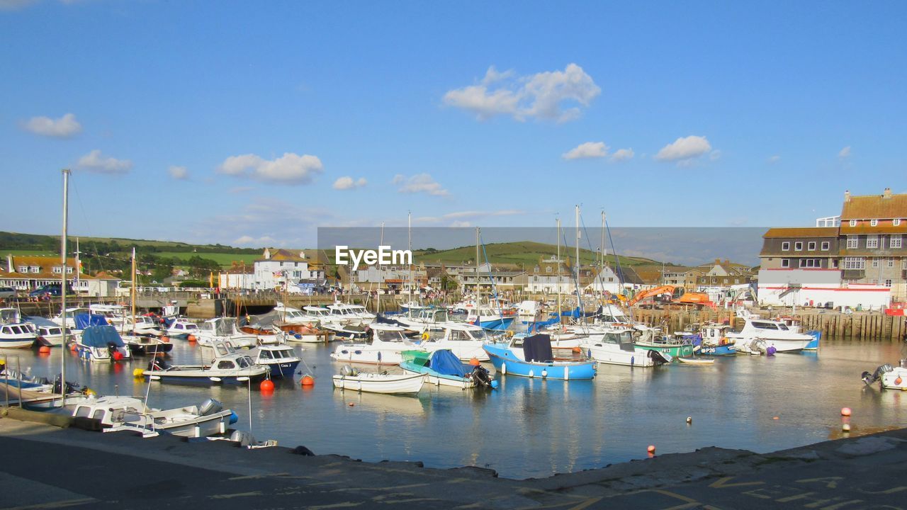 SAILBOATS MOORED AT HARBOR AGAINST SKY