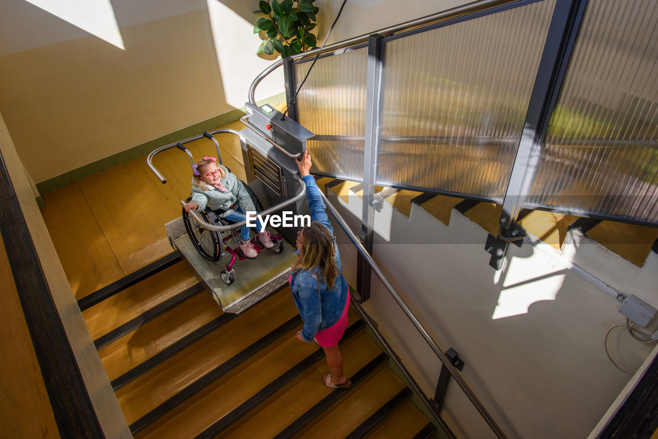 Mother and child living with cerebral palsy using wheelchair lift to access public building.