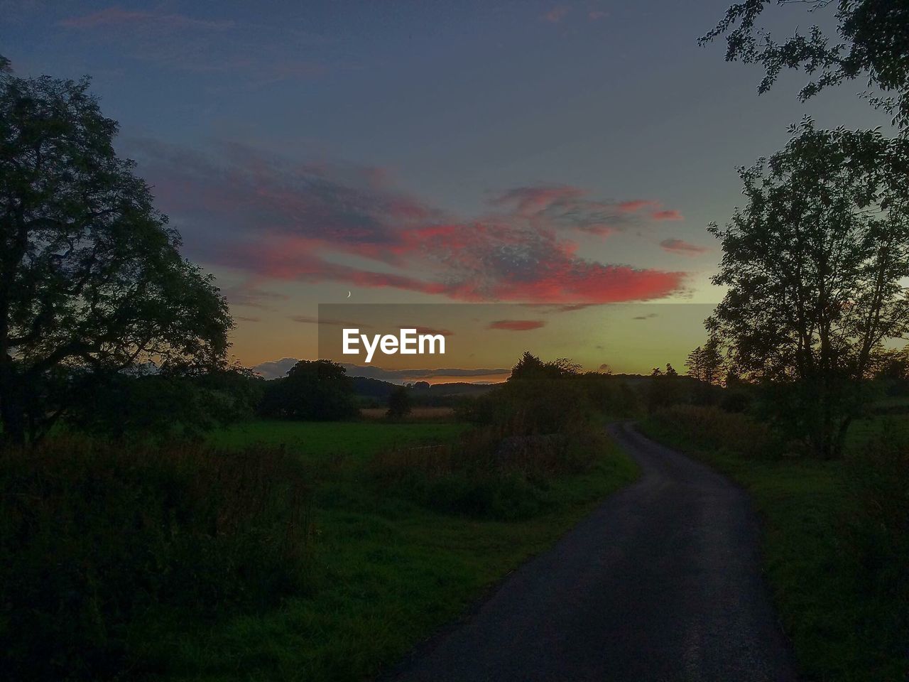 ROAD ON FIELD AGAINST SKY AT SUNSET