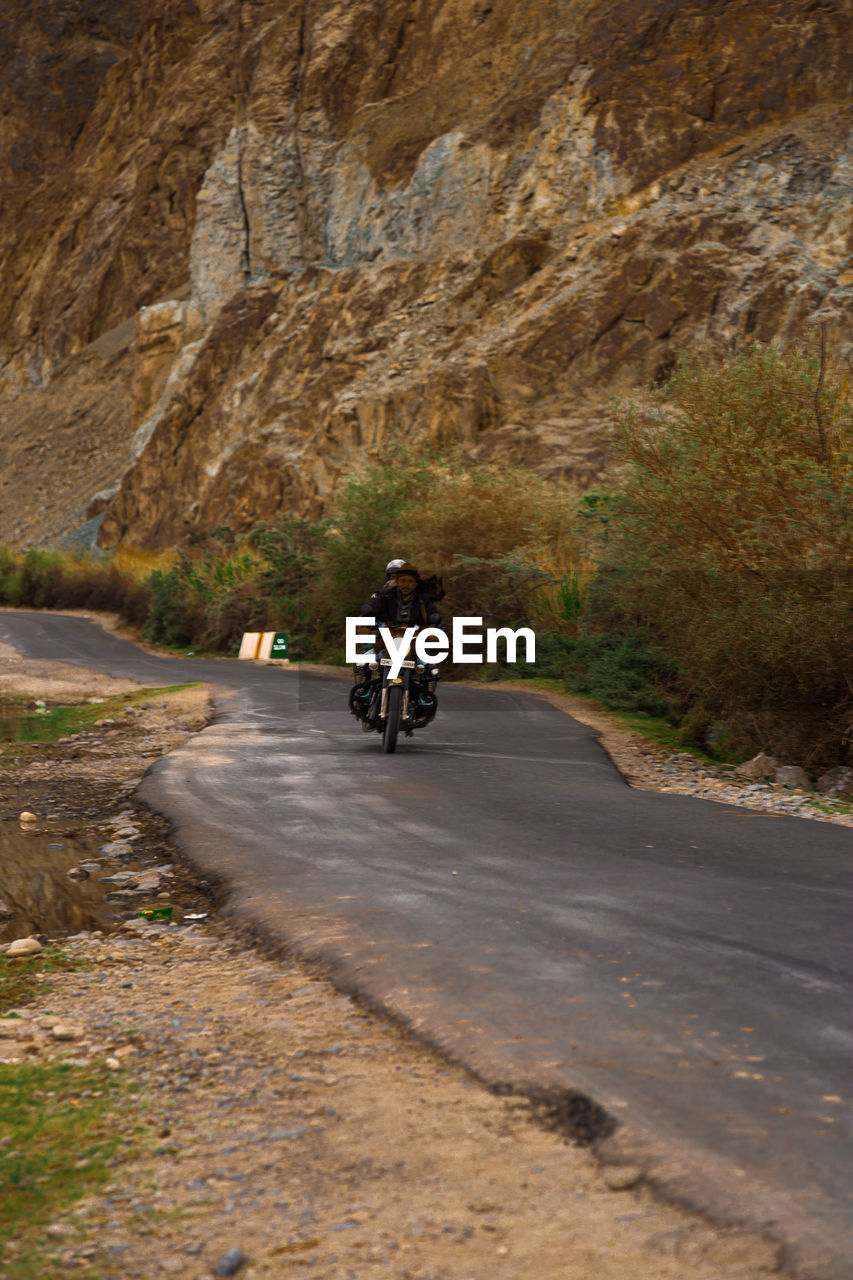 MAN RIDING MOTORCYCLE ON ROAD IN MOUNTAINS