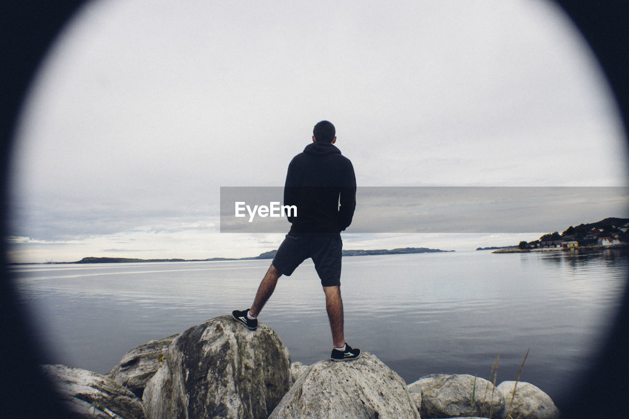 REAR VIEW OF MAN STANDING ON PIER AT SEA