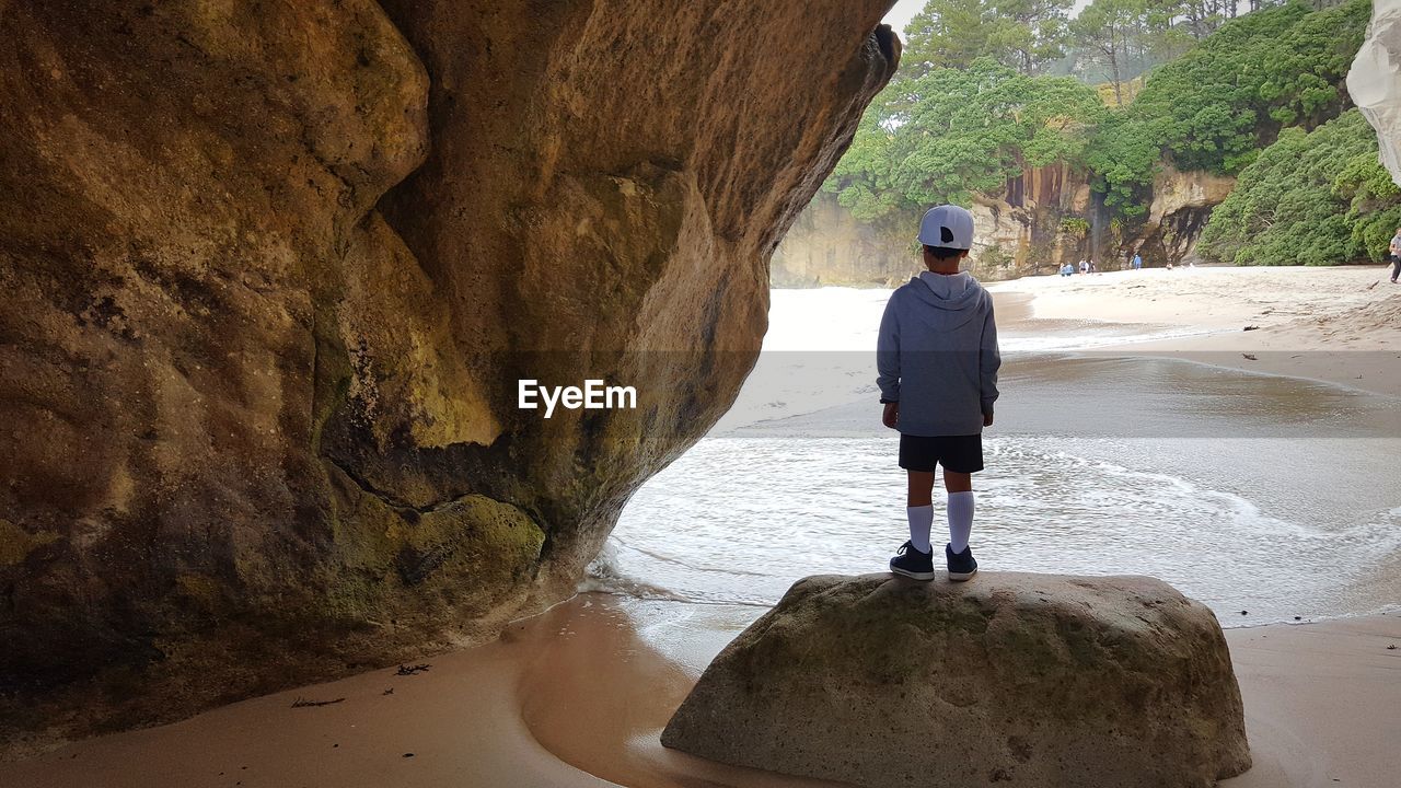 Rear view of boy standing on rock at beach