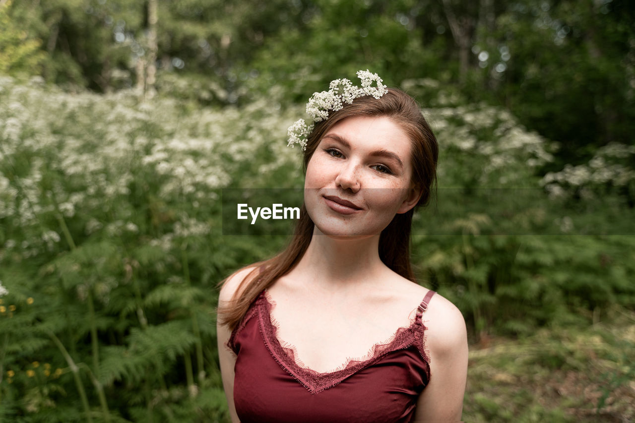 Portrait of smiling young woman standing against plants in park