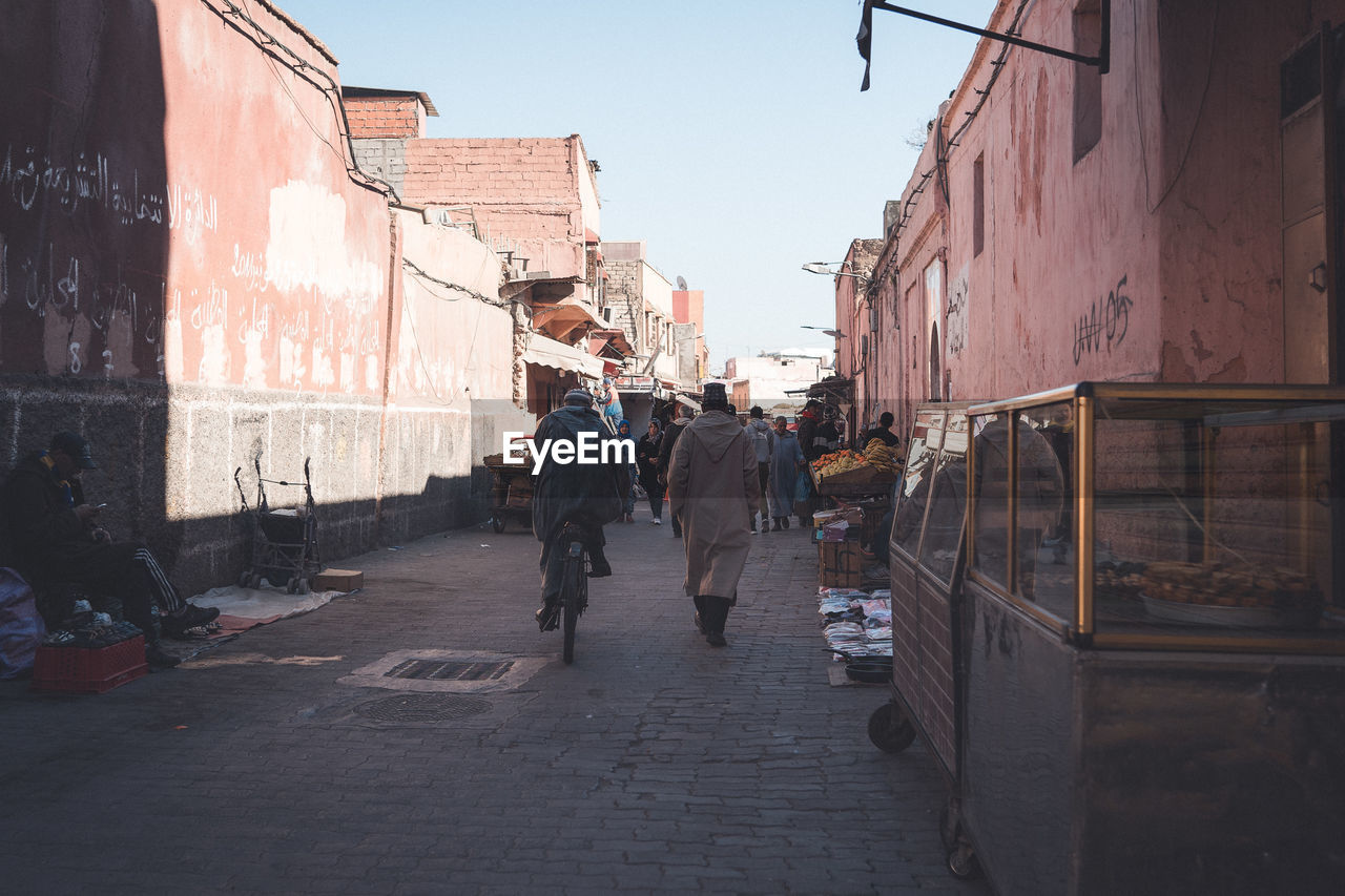 PEOPLE WALKING ON STREET AMIDST CITY BUILDINGS