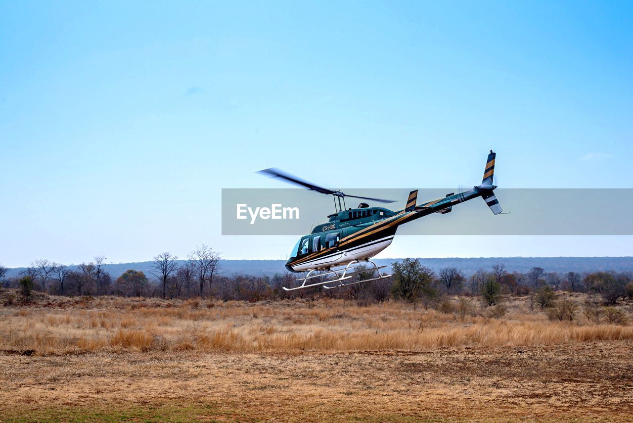 Helicopter on landscape against clear blue sky