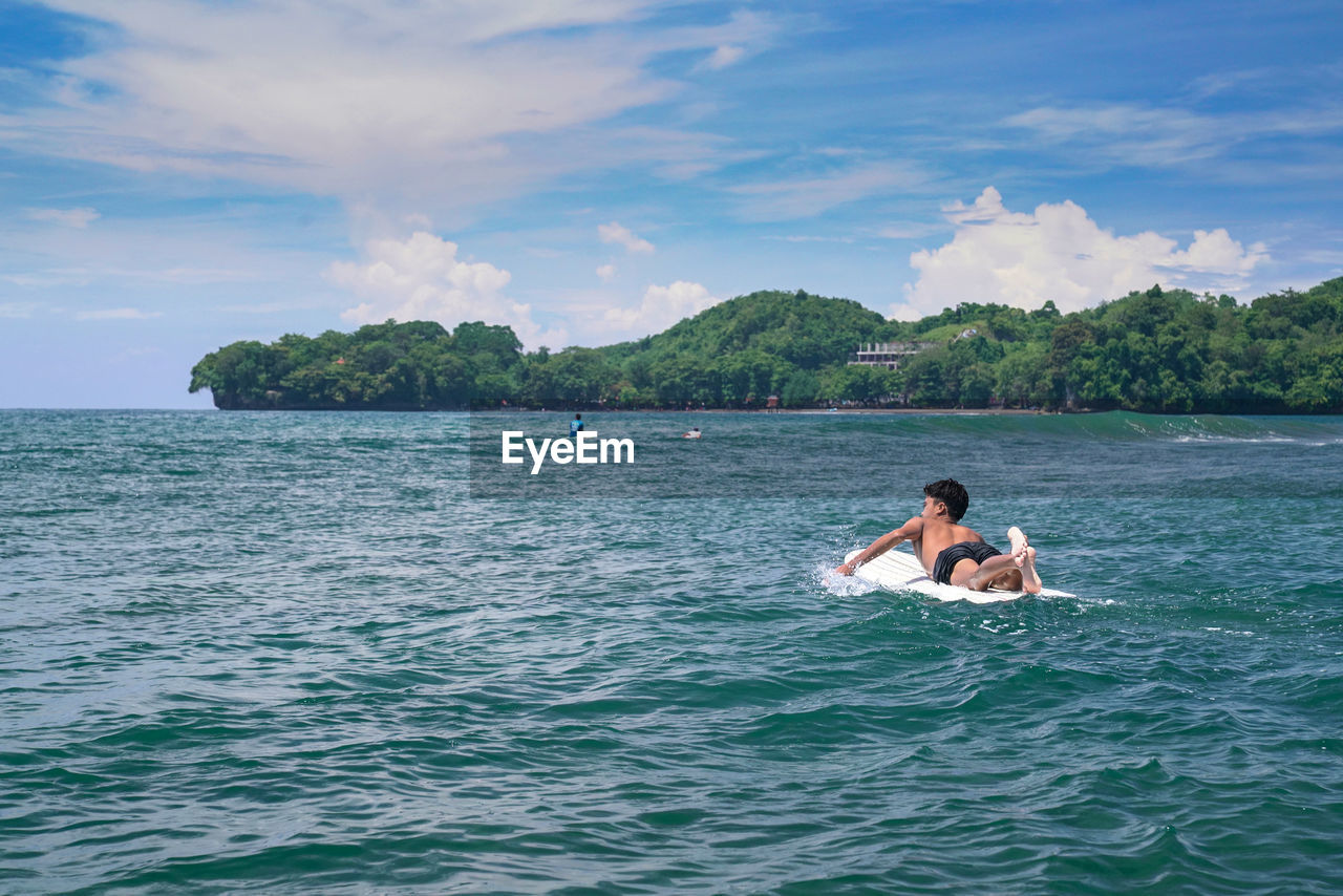 Surfer in sea against sky batu karas, pangandaran west java