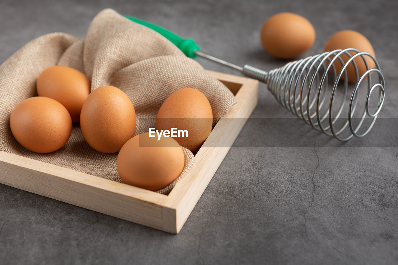 Chicken eggs and egg beater in the wooden tray on the black cement floor. high angle view.