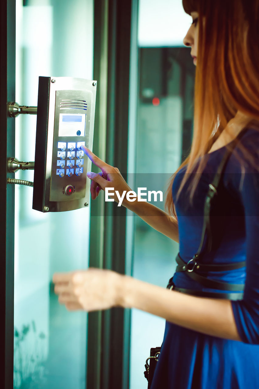 Side view of young woman using elevator buttons