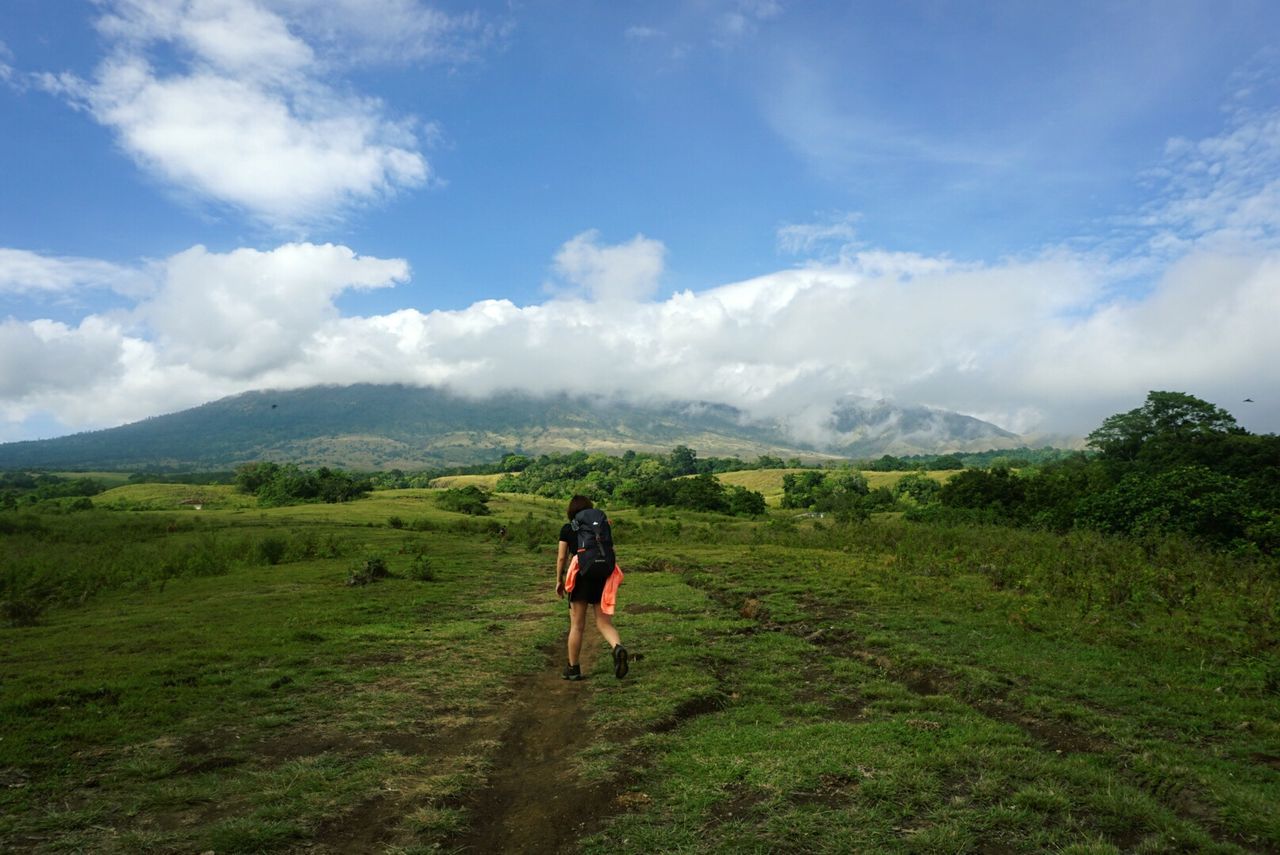 Rear view of female hiker walking on grassy field against sky