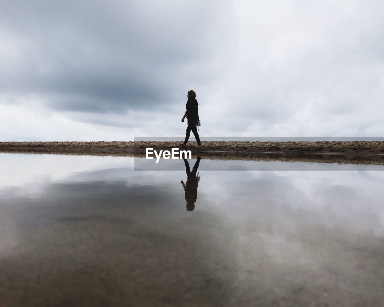 Side view of woman walking at beach against sky