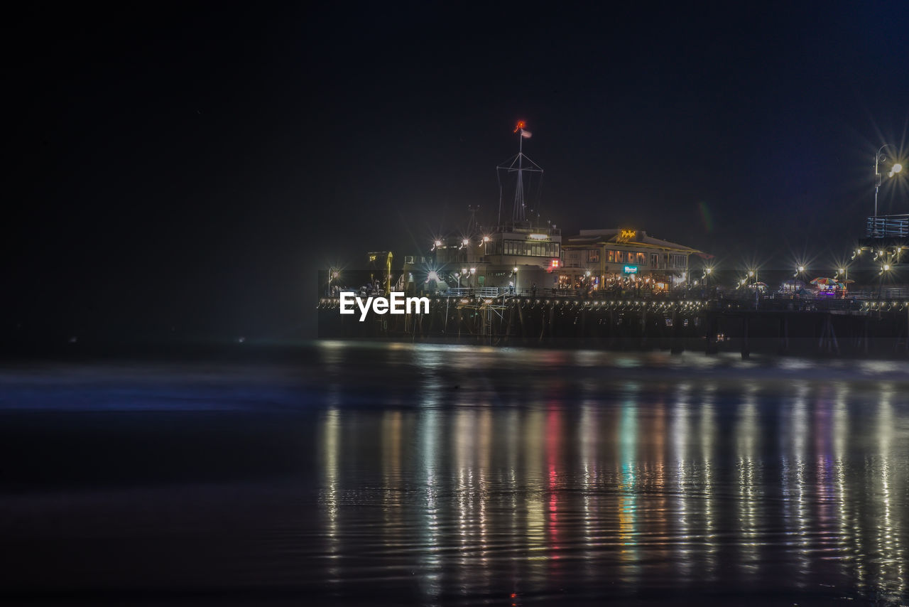 REFLECTION OF ILLUMINATED LIGHTS IN SEA AT NIGHT