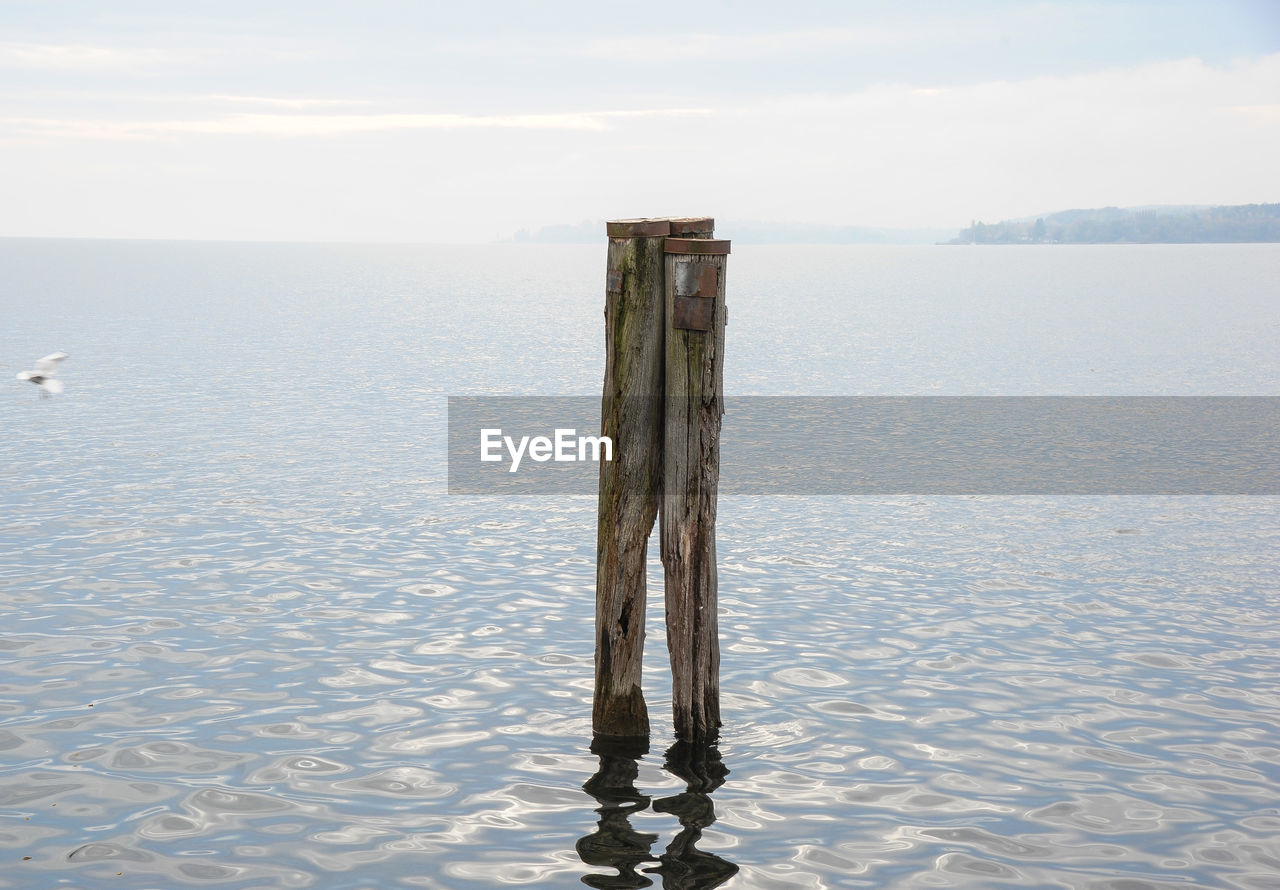 WOODEN POST ON SEA AGAINST SKY