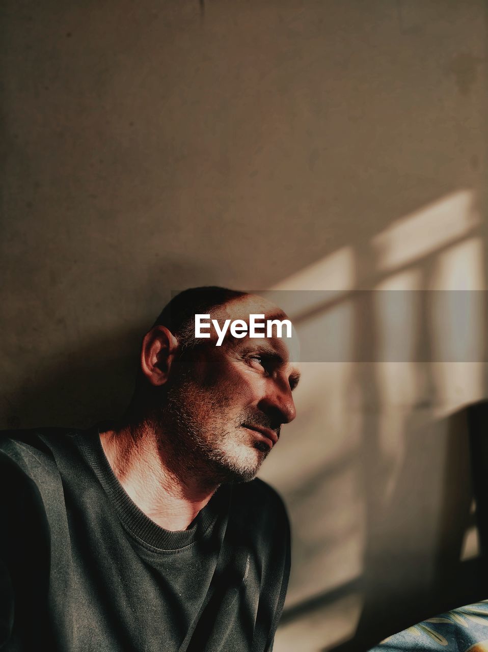 Mature man looking away while sitting against wall