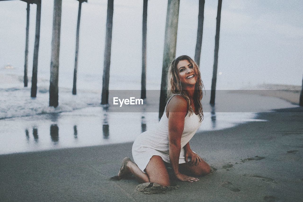 Portrait of smiling young woman kneeling at beach