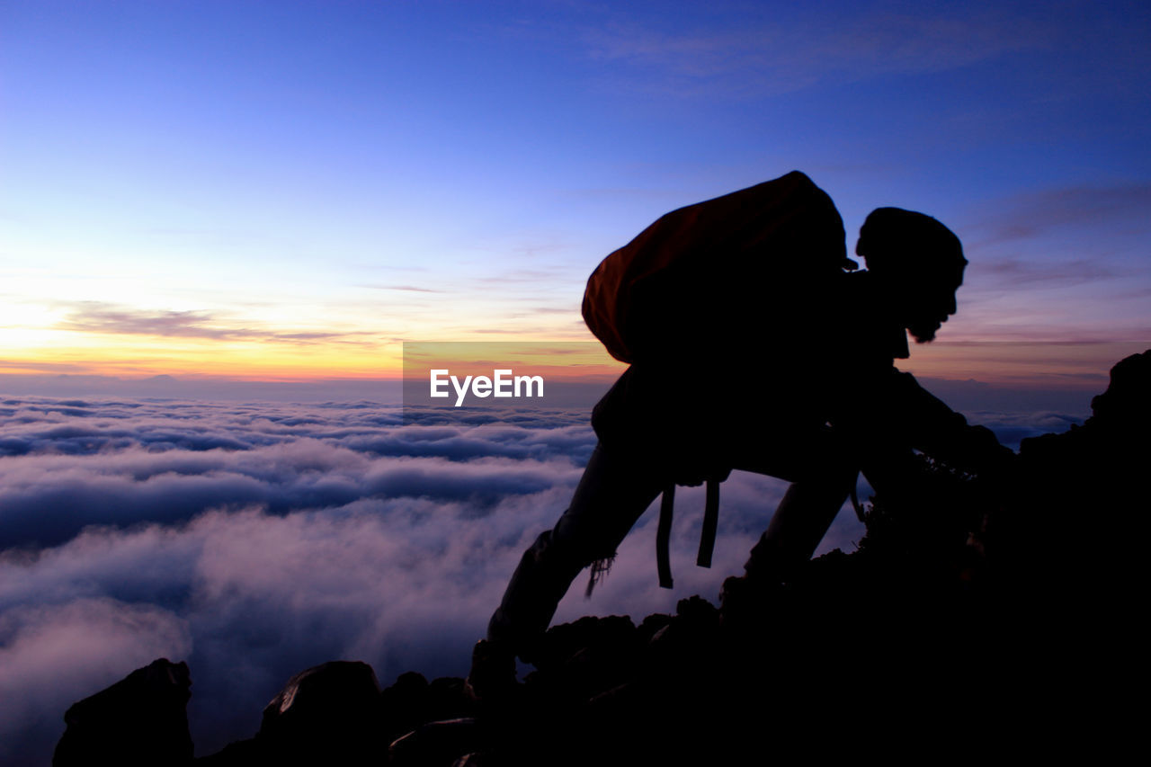 Man climbing on mountain against sky during sunset