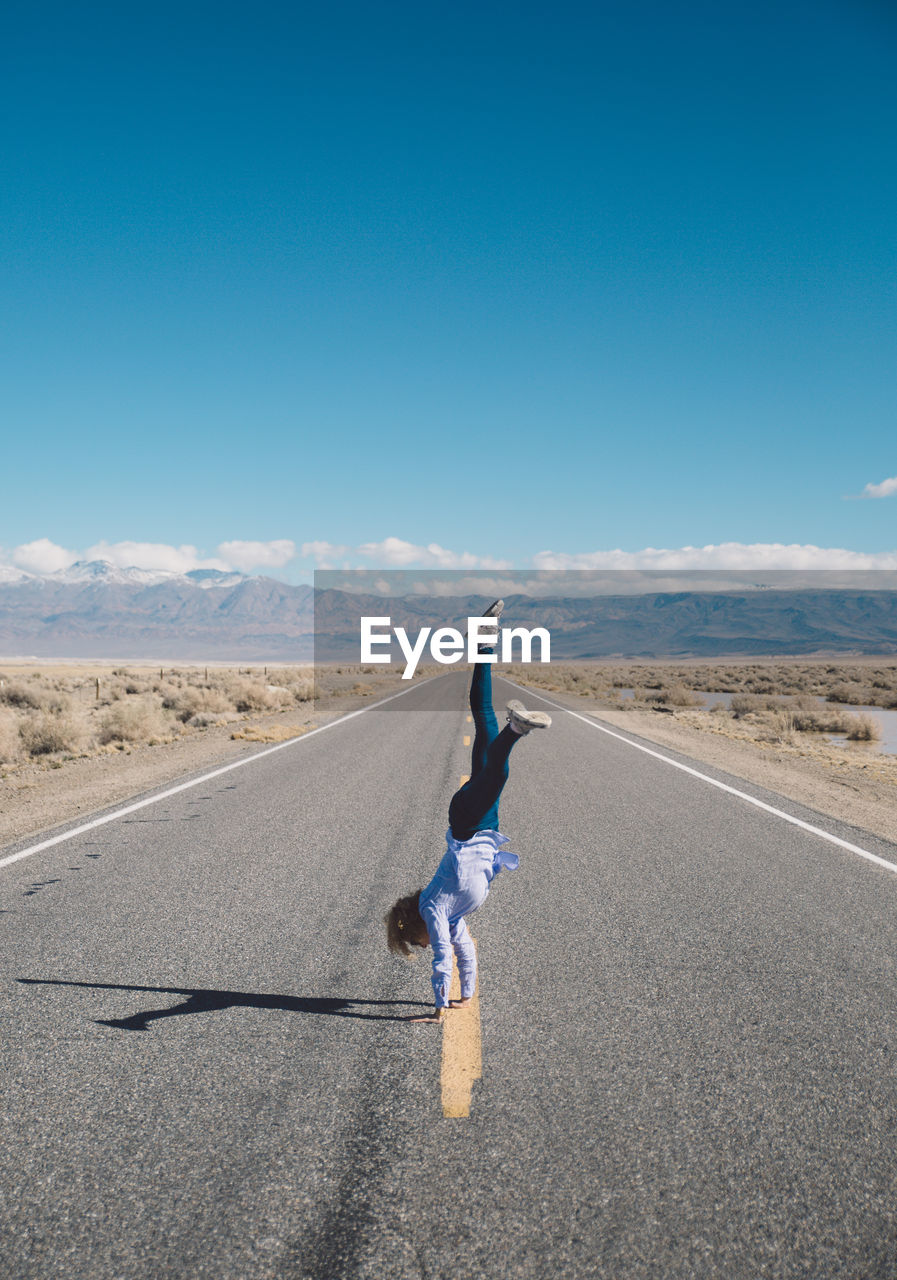 Woman doing handstand on road against clear blue sky