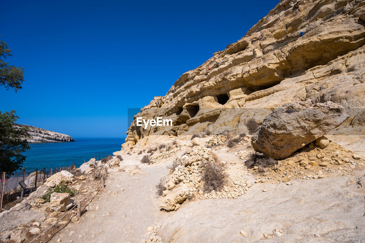 sky, nature, land, rock, scenics - nature, water, clear sky, beauty in nature, sea, blue, travel destinations, environment, wadi, landscape, travel, no people, tranquility, mountain, rock formation, beach, geology, coast, sunny, plant, tree, tranquil scene, day, cliff, outdoors, terrain, sunlight, non-urban scene, tourism, sand, formation