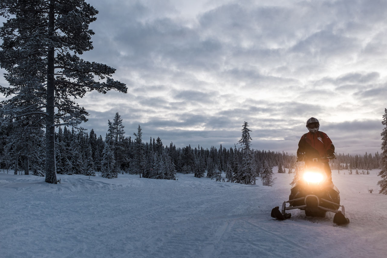 Man riding snowmobile on snow covered landscape against sky