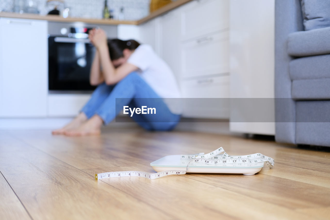 flooring, indoors, hardwood floor, home interior, domestic room, one person, wood, domestic life, floor, adult, footwear, living room, furniture, technology, casual clothing, lifestyles, young adult, men, person, full length, wood flooring, parquet floor, room, relaxation, hardwood, sitting, lying down, clothing, emotion, selective focus, looking