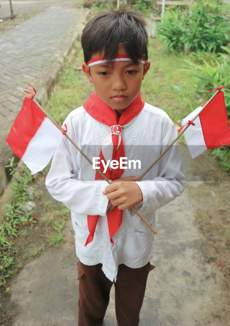 Boy holding indonesian flags while standing on field