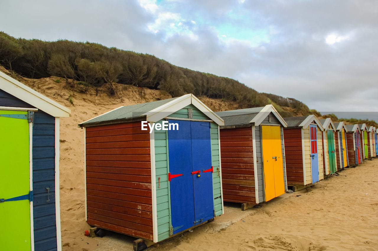 Beach huts by hill against sky