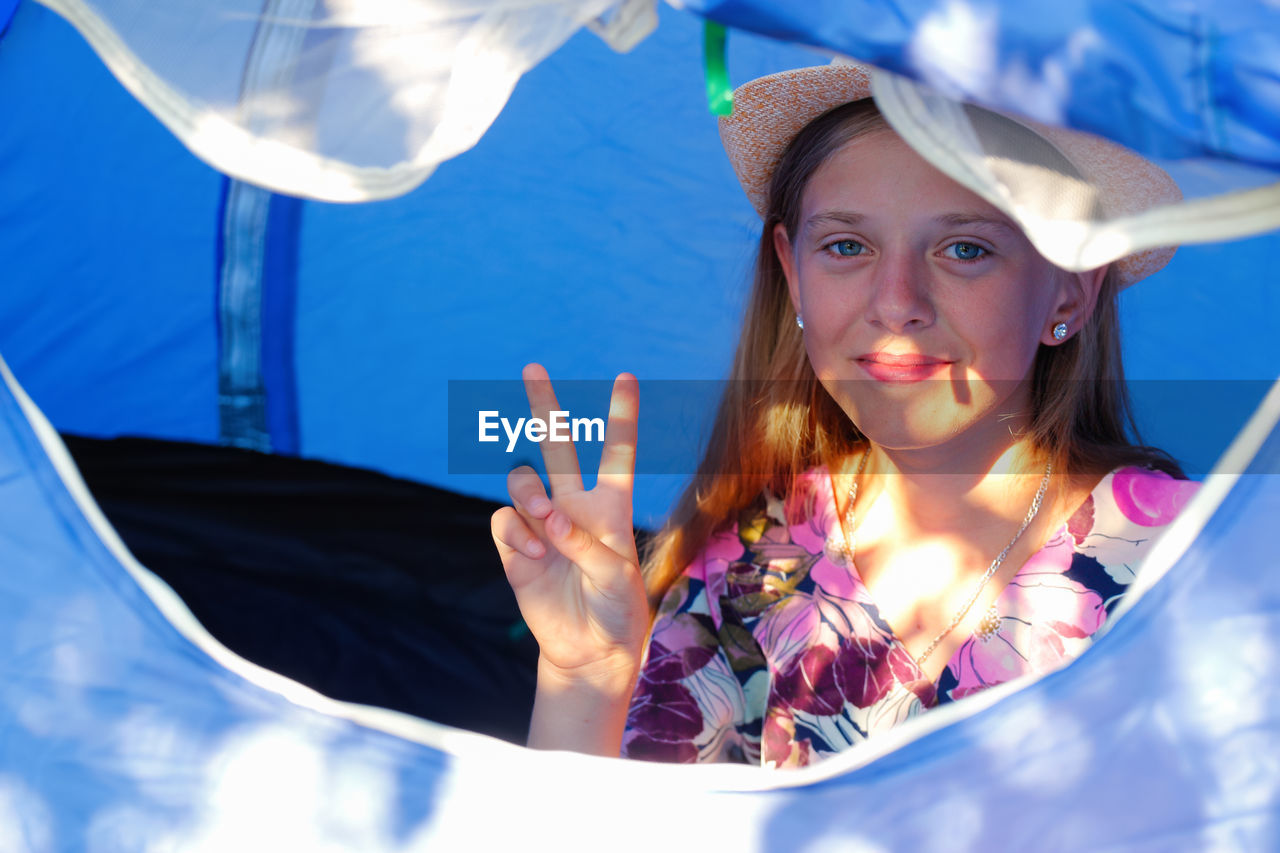 Girl sitting comfortably inside a camping blue tent behind a mesh anti-mosquito window, she looking