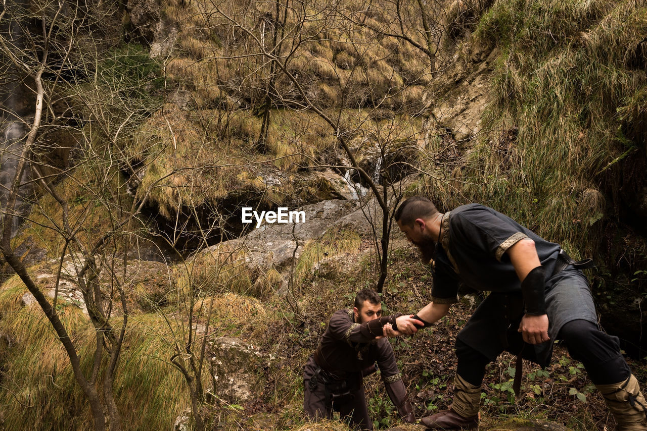 Warrior helping man climbing in forest