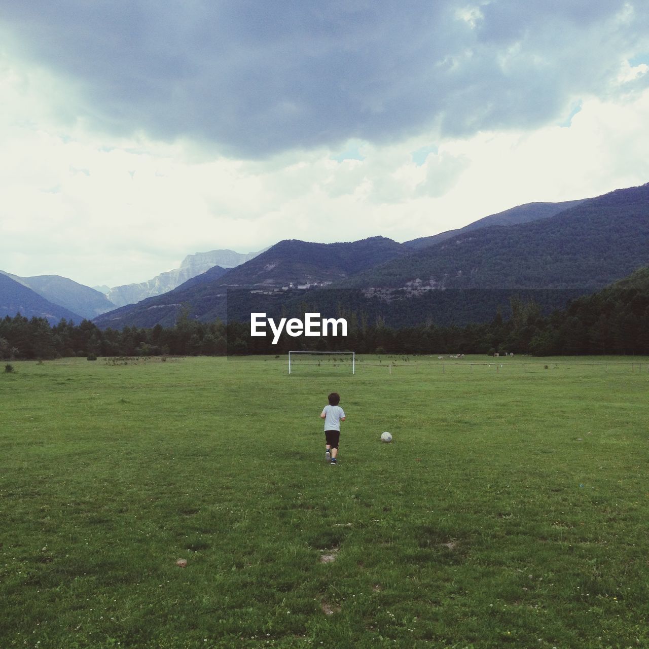 Rear view of boy playing soccer on field against sky