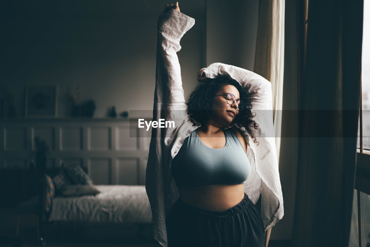 Curly haired plus size woman wearing comfortable clothes dances in stylish room.